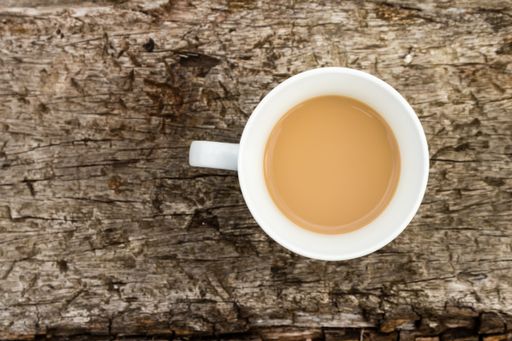 A high angle shot of a white cup of coffee on a wooden surface