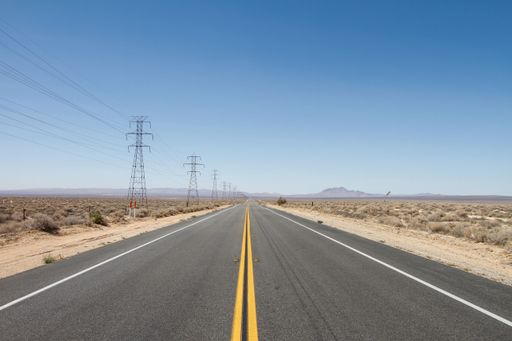 An empty highway road with dry plant fields on each side on a sunny day