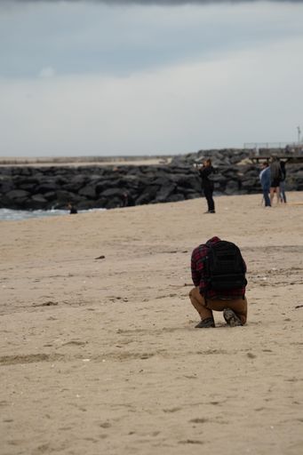 A man with a camera catching photos of sandy surface with gray sky on the horizon, vertical shot