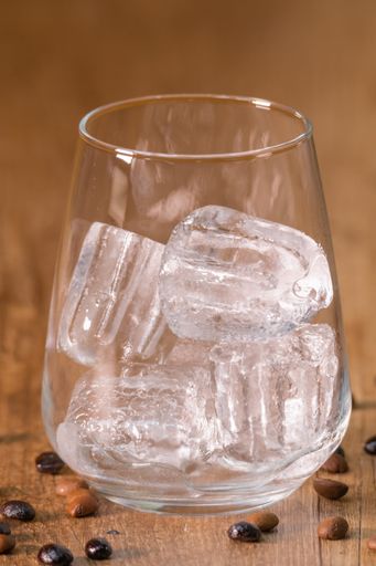 A vertical shot of ice cubes in a glass on a wooden table with roasted coffee beans on it
