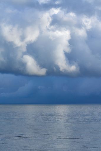 A landscape of blue sea with dramatic cloudy sky on the horizon, vertical shot