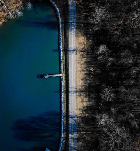 A drone shot over a road with forest trees by large blue lake on a sunny day in Memphis, Tennessee