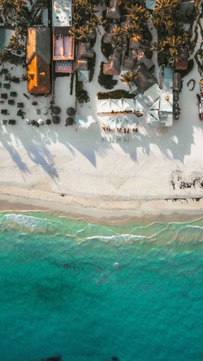 An aerial drone view of foamy waves crashing on a white sandy beach on a sunny day
