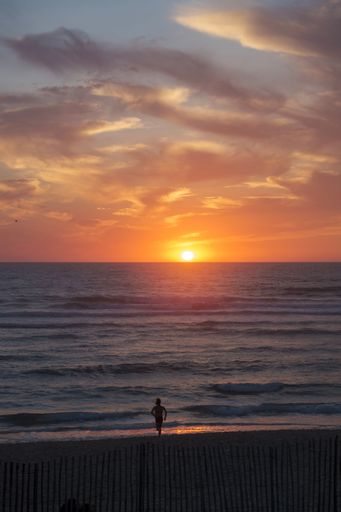 A man walking on the beach against the tranquil sea at sunset
