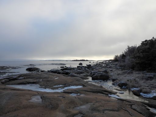 A scenic beach featuring a rocky shoreline with large chunks of melting ice against a clouded sky