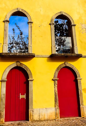 A vertical shot of a weathered old beautiful building with yellow walls and red arch doors