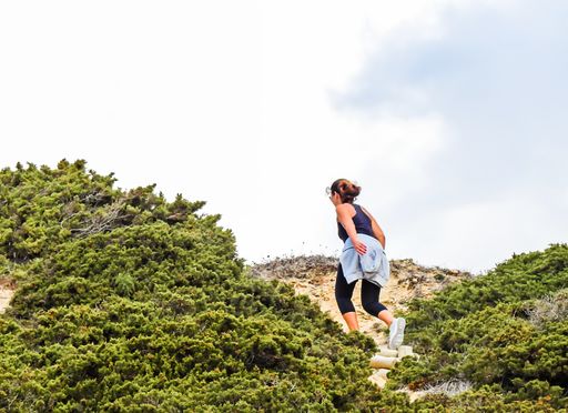 A low angle of an adventurous, sporty woman hiking a hill under the cloudy sky