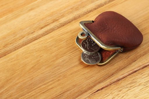 A high angle shot of a leather change purse and some coins on a wooden surface
