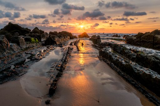 A dramatic sunset over the wet rocky seashore
