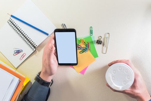 Top view of male hands holding a smartphone, on a desk with supplies. Business or educational concept.