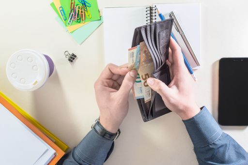 Top view of a male hand taking money out of a wallet, on a desk with office supplies