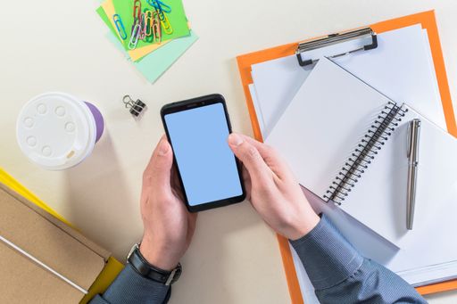 Top View of male hands holding a smartphone, on a desk with supplies Business or educational concept.