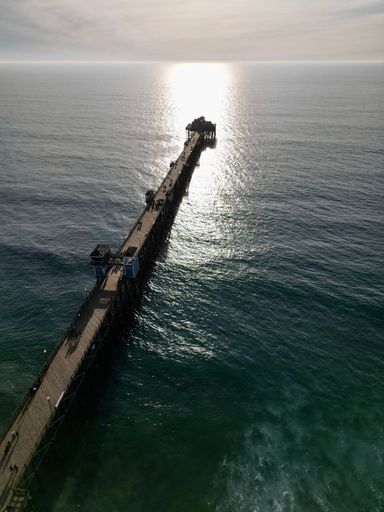 A pier with under bright sunlight over a calm blue-green sea in California