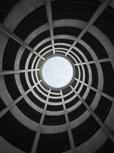 A low angle view of the ceiling of a building from inside with a spiraling pattern and a hole allowing sunlight through