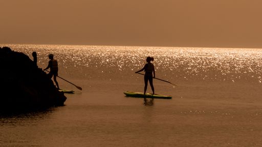 The silhouettes of two paddleboarders floating on the water illuminated by a stunning orange sunset