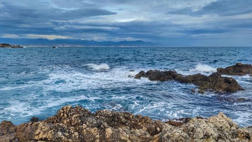 A scenic shot of sea waves slamming on a rocky beach under a cloudy gloomy sky