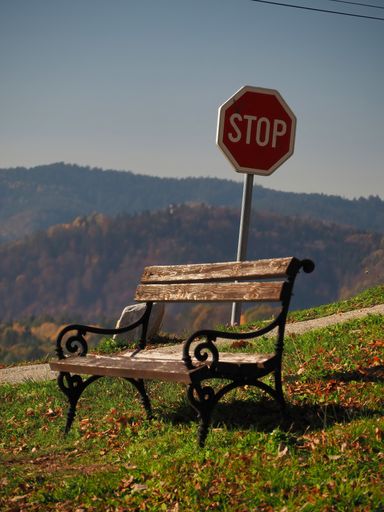 A vertical shot of a bench in a field with a road sign behind it under the clear sky - a sistop