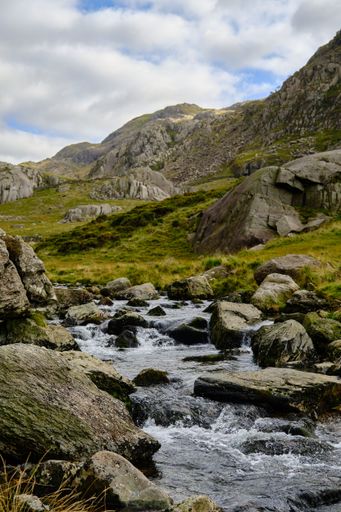 A vertical shot of a stream surrounded by rocks and greenery in the countryside