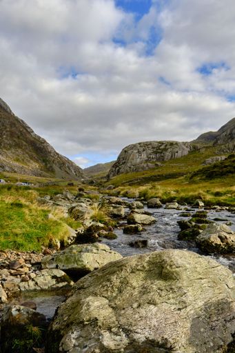 A vertical shot of a stream surrounded by rocks and greenery in the countryside