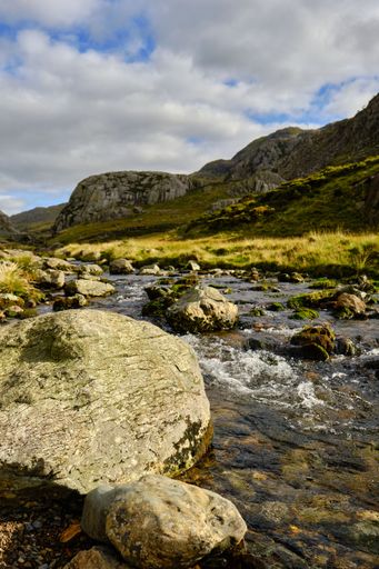 A vertical shot of a stream surrounded by rocks and greenery in the countryside