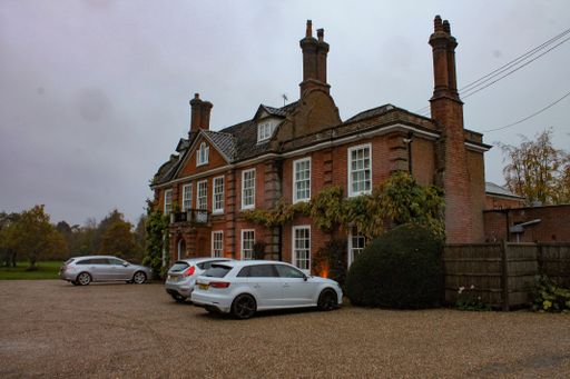 The two-story brick private house with windows with white bars and cars parking in the yard by the beautiful garden in London, UK
