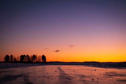 A scenic view of a frozen lake with trees in the background during a mesmerizing sunset
