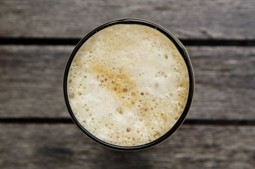 A high angle shot of a glass with coffee foam isolated on a wooden surface