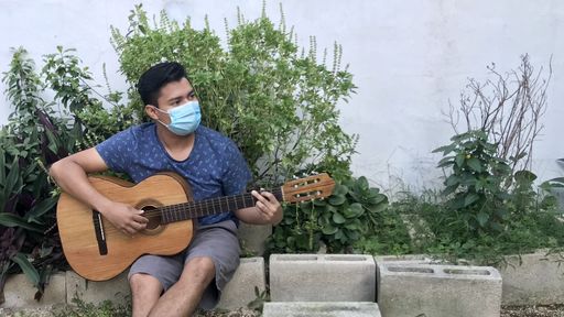 A Hispanic guy playing his guitar while wearing a face mask
