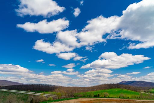 An aerial view of a rural countryside, surrounded by lush rolling hills and clouded blue sky in West Virginia