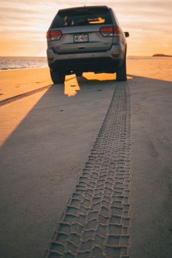 A vertical shot of a gray 2018 Jeep Grand Cherokee at the beach at sunset