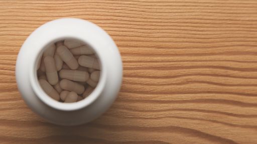 A high angle shot of capsules in a white container on a wooden surface