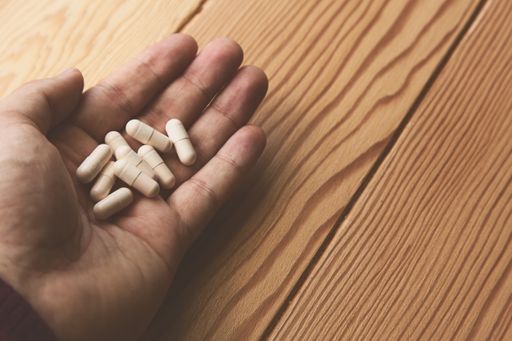 A high angle shot of a person holding a bunch of white capsules over a wooden surface