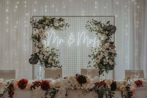 A table topped with flowers and greenery next to a neon sign with Mr and Mrs writings