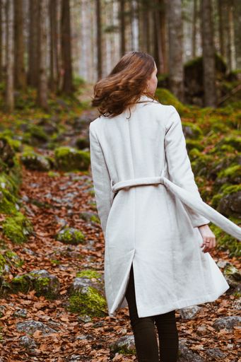 A vertical shot of a young Caucasian female walking in a forest wearing a white coat