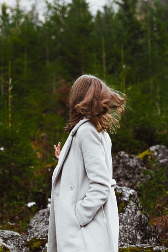 A vertical shot of a young Caucasian female walking in a forest wearing a white coat