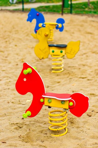 A vertical selective focus shot of spring rockers in a sandy playground