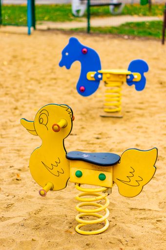 A vertical selective focus shot of spring rockers in a sandy playground