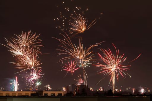 An illuminated night sky filled with vibrant fireworks explode above a cityscape of buildings