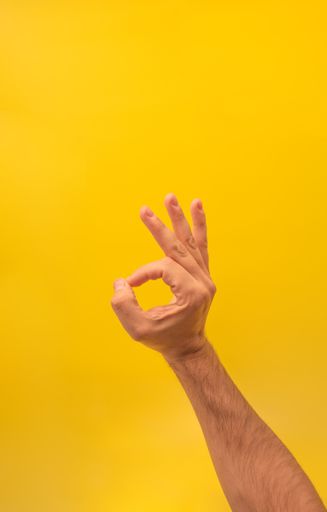 A male hand showing the OK sign on a yellow background