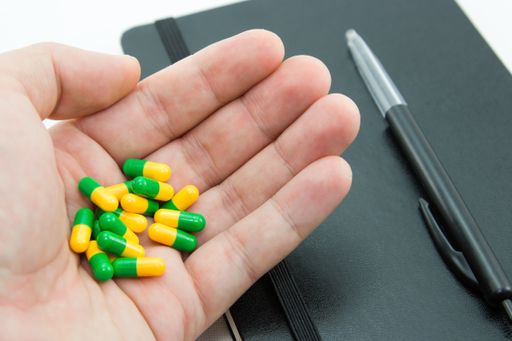 A high angle shot of a person holding some capsules over a notebook and a pen