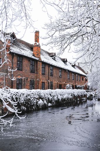 A vertical shot of a brick building next to a river in winter covered in white snow in London