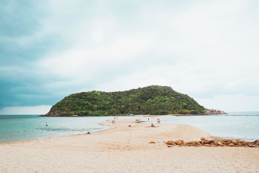 A sandy beach with a small island in the middle of the ocean on a sunny day