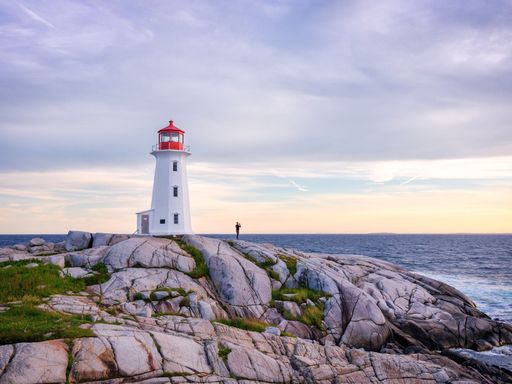 A lighthouse perched atop a rocky cliff, illuminated by the vibrant pink hues of a setting sun