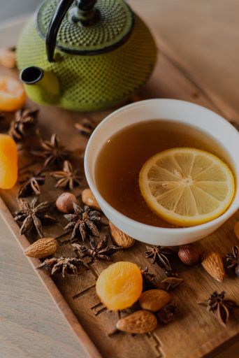 A close-up shot of a vintage green teapot and dry fruits and a tea with lemon in a cup