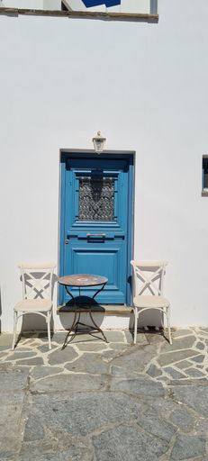 A vertical shot of a blue wooden door with a small table and two chairs in front of it during daytime in a street