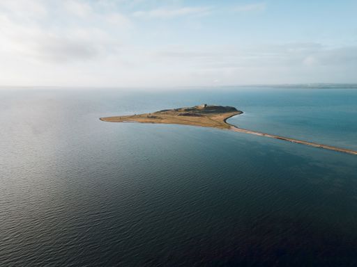 An aerial view of an island with the Kalo Castle barely visible on  the water in Denmark