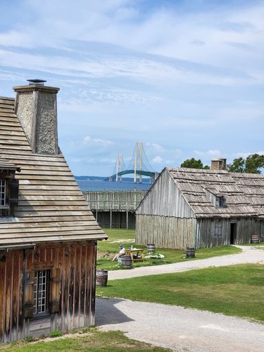 A vertical shot of a woman sitting by small buildings at Fort Michilimackina in Mackinaw, Michigan, USA
