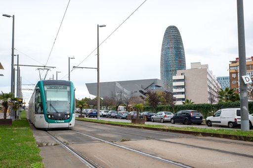 A high-speed passenger train zooming past a bustling city street in Barcelona