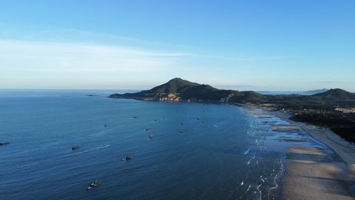 A drone view of the seascape surrounded by hills and a sandy shore with people in the daytime