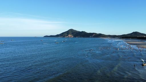 A drone view of the seascape surrounded by hills and a sandy shore with people in the daytime